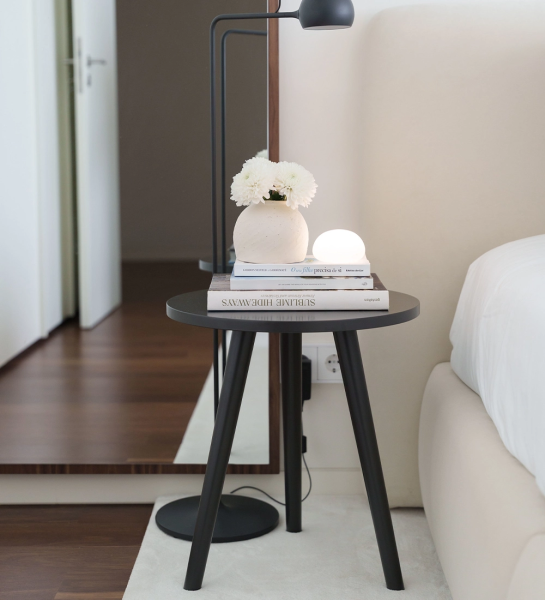 Mesa Auxiliar Oslo redonda marrón junto a cama con libros y jarrón